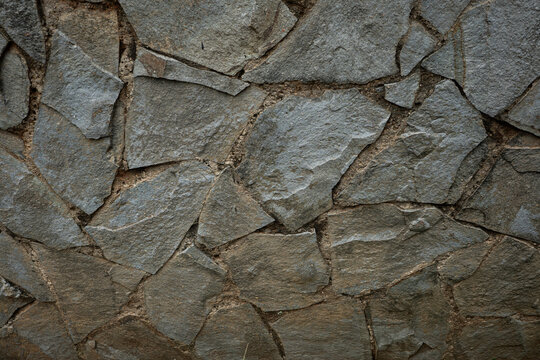 Close-up of irregular stone wall with rough texture and earthy tones, creating a natural and rustic pattern ideal for backgrounds or architectural design - Powered by Adobe