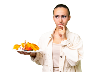 Young Arab woman holding waffles over isolated background having doubts and thinking
