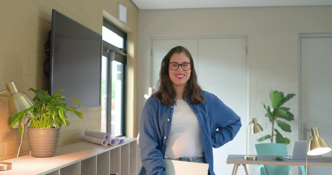 Woman holding folder as camera zooming in, smiling and laughing, showing confidence in workroom