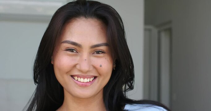After brief pause Asian woman smiling then laughing in entryway against wall with air conditioner