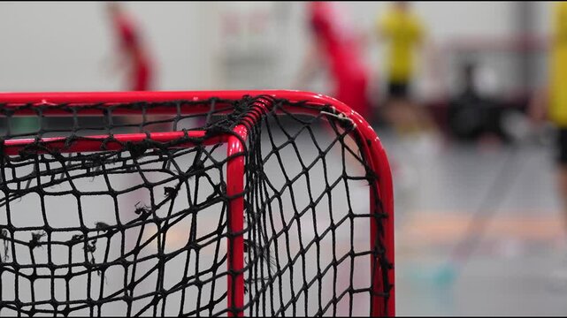 Valmiera, Latvia - December 03, 2025: Floorball net in focus as players engage in fast-paced action, camera zooms in to capture intensity