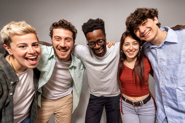 Studio shot of cheerful diverse young adults standing in line and embracing each other with big smiles