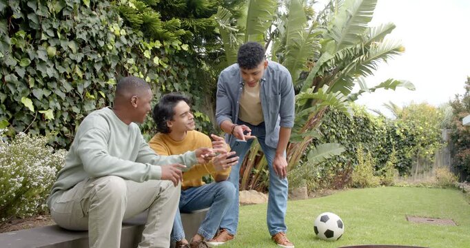 Spotting soccer clip triggers diverse male friends tapping smartphone on backyard bench pointing