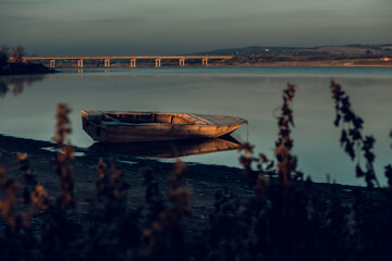 Serene lakeside scene with a wooden boat at sunset, reflecting calm waters and peaceful mood