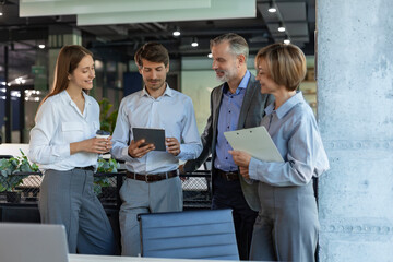 Group of business people standing together and discussing their work and projects, having a team meeting in an office.
