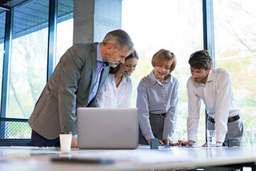 Four business professionals using laptop on desk discussing strategy company