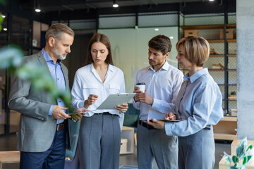 Group of business people standing together and discussing their work and projects, having a team meeting in an office.