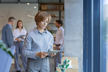 Pretty middle aged businesswoman uses digital tablet standing in the office.
