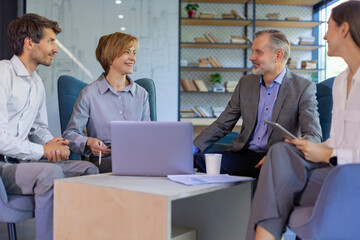 Four business professionals using laptop on desk discussing strategy company