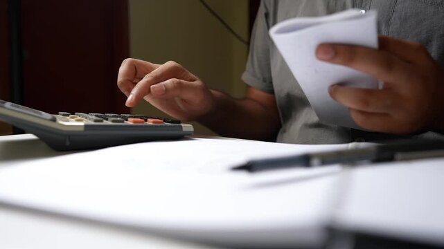 Person using a calculator with a notepad and pen on a desk shot