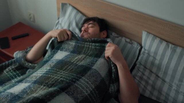 Tired man lifting blanket to hide his face during a dull early morning