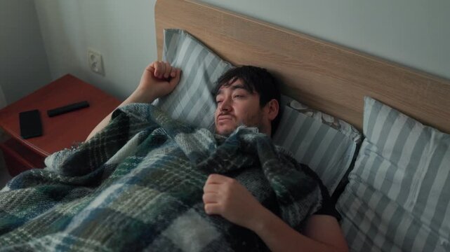 Tired man lifting blanket from his face during a slow early morning wake-up