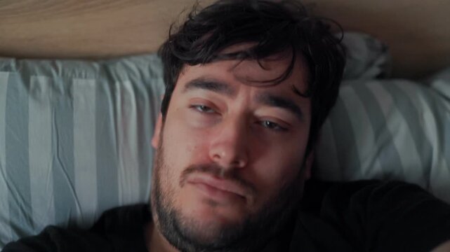 Exhausted man falling back onto bed with a tired expression in a morning scene