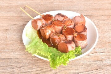 pork sausage roll up bacon stabbing plant stick dressing spicy barbecue sauce arranging with vegetable on plate