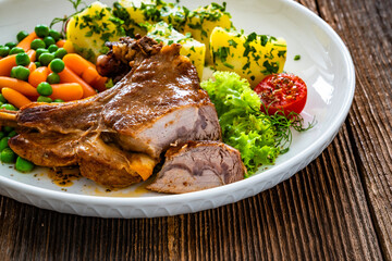 Baked veal cutlet with bone, boiled potatoes, mini carrots and green peas on wooden table