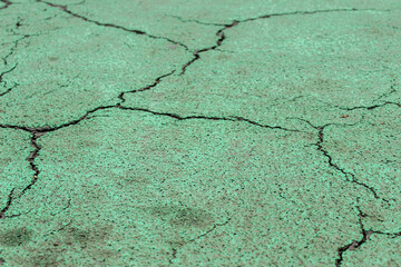Obraz premium Cracked teal green asphalt surface with small grain texture, showing severe damage and large, spreading fracture lines.