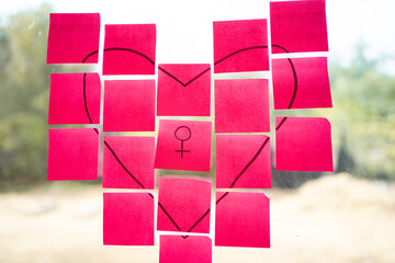 Pink sticky notes forming a heart shape with female symbol on glass window