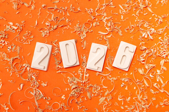 Сlose-up of the white numbers 2026 on a orange background with sawdust