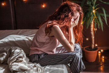 Sad young woman lying in bed
