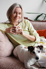 Happy middle aged Woman sitting with Dog on Sofa in living room with cup of tea or coffee