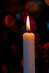 Candle flame glowing against dark background. Spiritual concept of hope and peace. Blurred red...