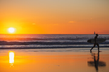 Surfer Walking Through Golden Sunset Reflections , Caravelos beach, Portugal