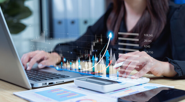 Businesswoman using laptop and calculator to review company growth with upward trend graphics, analyzing financial data, future development, and long-term investment outlook.