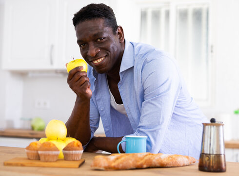 Positive African American eating apple in cozy kitchen interior at home - Powered by Adobe