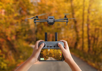Aerial drone hovering above an autumn forest road, controlled from a handheld remote displaying a live video feed for filming and monitoring © Stanisic Vladimir