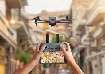 Drone hovering above a busy city street while the pilot monitors the live video feed on the controller for filming and urban surveillance.