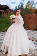 Bride in elegant white dress holding bouquet on wooden platform by water at sunset