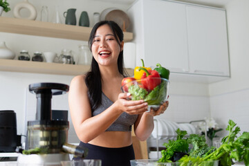 A young woman holds a cup containing various vegetables, preparing to make vegetable juice in the kitchen.