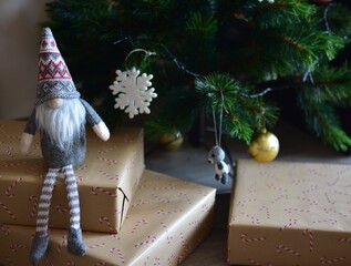 Cozy Christmas scene with a small Nordic gnome sitting on wrapped gifts under a decorated tree. Kraft paper boxes, soft handmade toy and natural holiday decor create a warm festive atmosphere at home.
