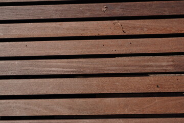 Fototapeta premium An architectural close-up of horizontal reddish-brown wooden slats, featuring a fine natural grain, uniform spacing, and rhythmic linear shadows between the planks.