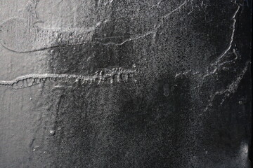 A high-contrast macro shot of a black industrial paint surface, featuring a complex mixture of matte textures, glossy splatters, viscous drip marks, and fine air bubble craters.