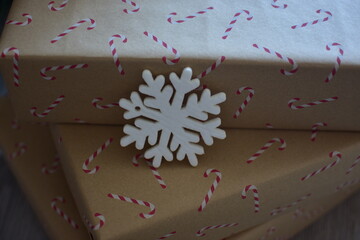 Close-up of kraft paper wrapped presents with red candy cane pattern, decorated with a white snowflake. Simple and warm eco-friendly Christmas packaging in natural festive style.