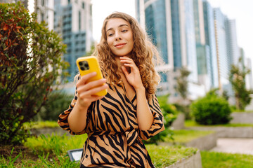 A portrait of a young woman smiling with a phone, standing against the backdrop of a metropolitan...