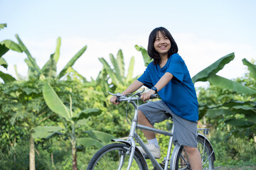 Girl riding a bicycle happily in a lush green outdoor environment.
