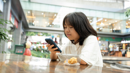 A young girl looking at her smartphone while sitting in a bright indoor area.