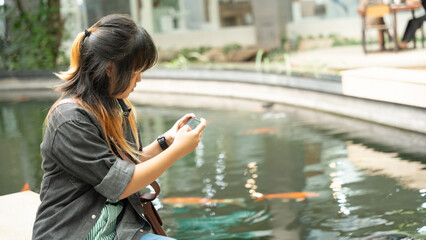 A young girl holding and looking at her phone near a koi pond.