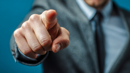 Man in formal attire pointing his finger directly at the camera with a focused expression against a solid blue background in a professional setting