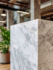 Elegant white marble pedestal with natural veining showcased in a contemporary industrial interior featuring exposed concrete columns and lush green plants