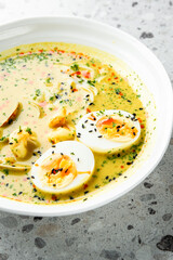 Vibrant yellow coconut curry noodle soup served in a white bowl with soft-boiled eggs, fresh herbs, and black sesame seeds, captured in a close-up shot.