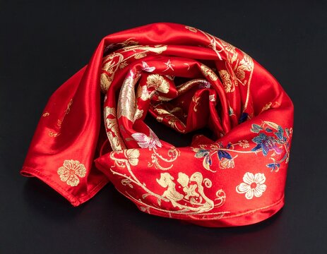A vibrant red silk scarf with intricate gold and blue floral patterns, elegantly rolled on a dark background. - Powered by Adobe