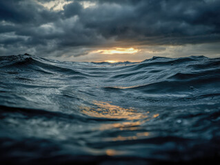 Dark stormy ocean waves under a dramatic cloudy sky with golden sunlight breaking through the horizon creating a moody seascape atmosphere at dusk