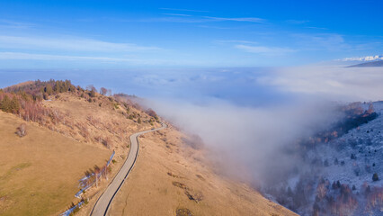 Aerial photography of a mountain plateau in winter season. Photography was taken from a drone at a higher altitude, above the clouds with a curvy road under. 