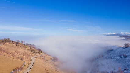 Aerial photography of a mountain plateau in winter season. Photography was taken from a drone at a higher altitude, above the clouds with a curvy road under. 