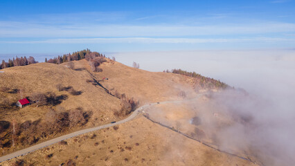 Aerial photography of a mountain plateau in winter season. Photography was taken from a drone at a higher altitude, above the clouds with a curvy road under. 