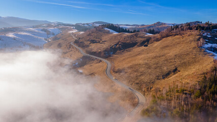 Aerial photography of a mountain plateau in winter season. Photography was taken from a drone at a higher altitude, above the clouds with a curvy road under. 