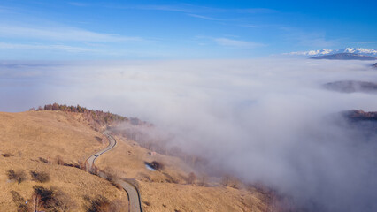 Aerial photography of a mountain plateau in winter season. Photography was taken from a drone at a higher altitude, above the clouds with a curvy road under. 